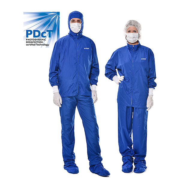 A man is standing on the left, a woman on the right. Both are wearing blue protective pants, a protective jacket and blue protective covers for the shoes. In addition, both are wearing white protective gloves and a white mouth guard. The man has the hood of the jacket on his head and the woman wears a white protective hood. On the left side of the chest, both have "ortner" written on them. On the left behind the man is a drawn blue square. From the upper right corner white rays go towards the lower left corner and also up and down. The square also says "PDcT" and "Photodynamic Disinfection certified Technology".
