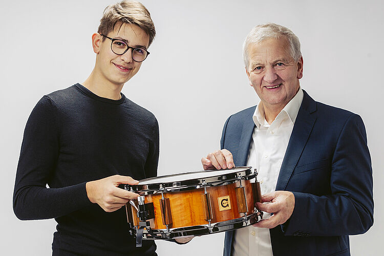 On the left is a young man, on his right is Josef Ortner. Both are holding a drum together.