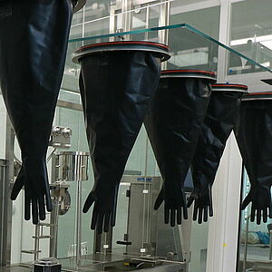 Zoom auf zwei nach oben geklappte Frontscheiben des Isolators. Von der rechten hängen vier schwarze lange Handschuhe nach unten. Von der linken Scheibe hängt einer.