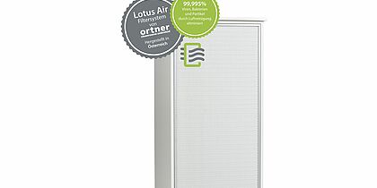  The upper part of a white box. A white wooden frame with a front that consists of a white fine grid. In the upper left corner are two circular stickers that cover the corner of the box. One is gray and one is green and something in the foreground. On the grey one it says 'Lotus Air filter system by ortner cleanrooms unlimited. Made in Austria' On the green one it says '99.995% viruses, bacteria and particles eliminated by air purification' Below that is a rectangular sticker of a green frame that is open a bit on the right side. To the left of the frame, three short gray strokes come out. To the right of the left stroke of the green frame, three wavy gray strokes go to the right. These extend beyond the opening of the green frame. Translated with www.DeepL.com/Translator (free version)
