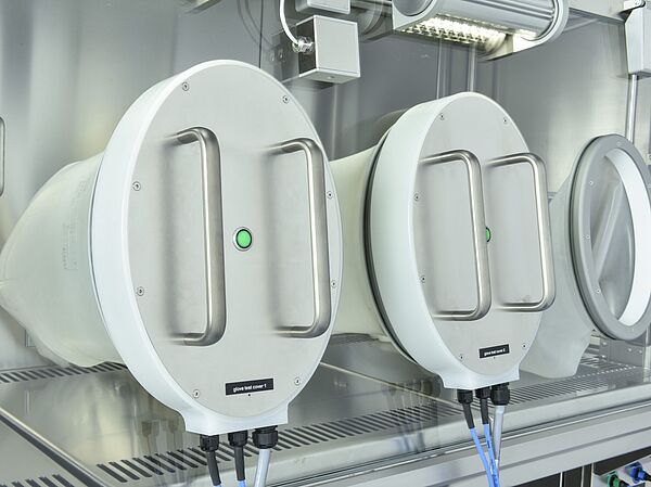 In der geschlossenen Frontscheibe eines Isolators sind zwei weiße Scheiben angebracht. Auf der Außenseite sind je zwei Griffe, an der Innenseite ist je ein weißer Handschuh, der in die Innenkammer des Isolators ragt. Rechts neben den beiden weißen Scheiben ist ein Kreis angebracht, an dem ebenfalls ein Handschuh in die Innenkammer des Isolators ragt.