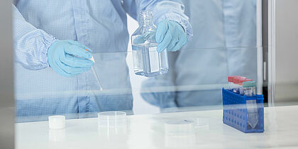 Two blue gloved hands holding a blue glass container and in the other hand holding a syringe