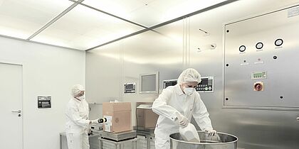 A photo of two people wearing white protective clothing working inside a ventilation system