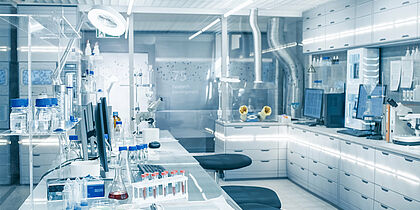 Ein Labor in dem Bildschirme, Mikroskope und unterschiedliche Flaschen stehen.
