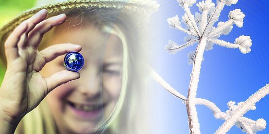 Ein Mädchen mit Hut hält eine kleine blaue Glaskugel vor ihrem Gesicht. auf der rechten Seite des Bildes ist auf blauen Hintergrund ein verschneiter Ast.