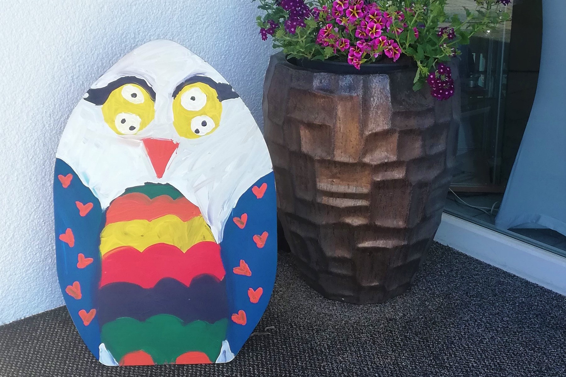 A colorfully painted wooden panel in the shape of an owl standing at the main entrance in Villach.